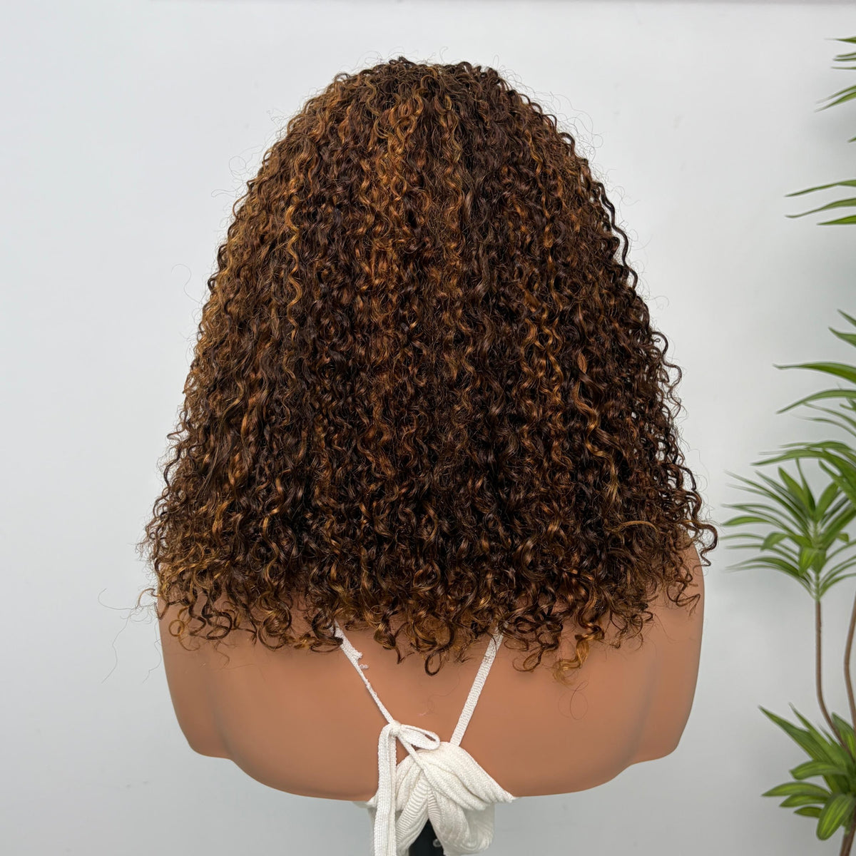 Perruque Olahair mi-longue à boucles serrées brun profond avec reflets caramel sur mannequin, vue de dos